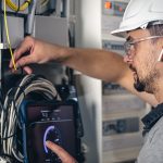 Man, an electrical technician working in a switchboard with fuses. Installation and connection of electrical equipment. Professional uses a tablet.
